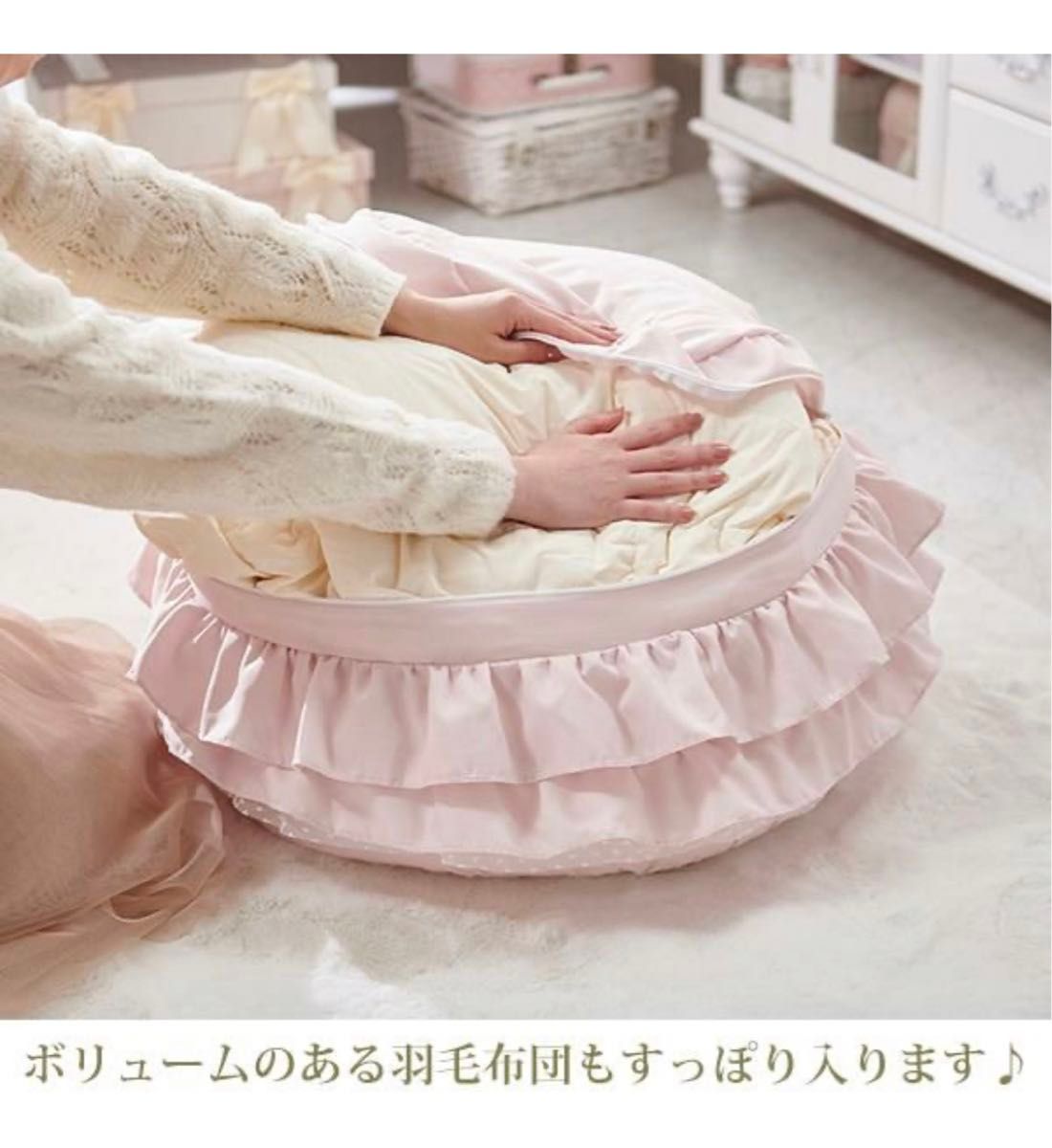 Hands placing a blanket into a pink ruffled blanket storage cover on the floor.