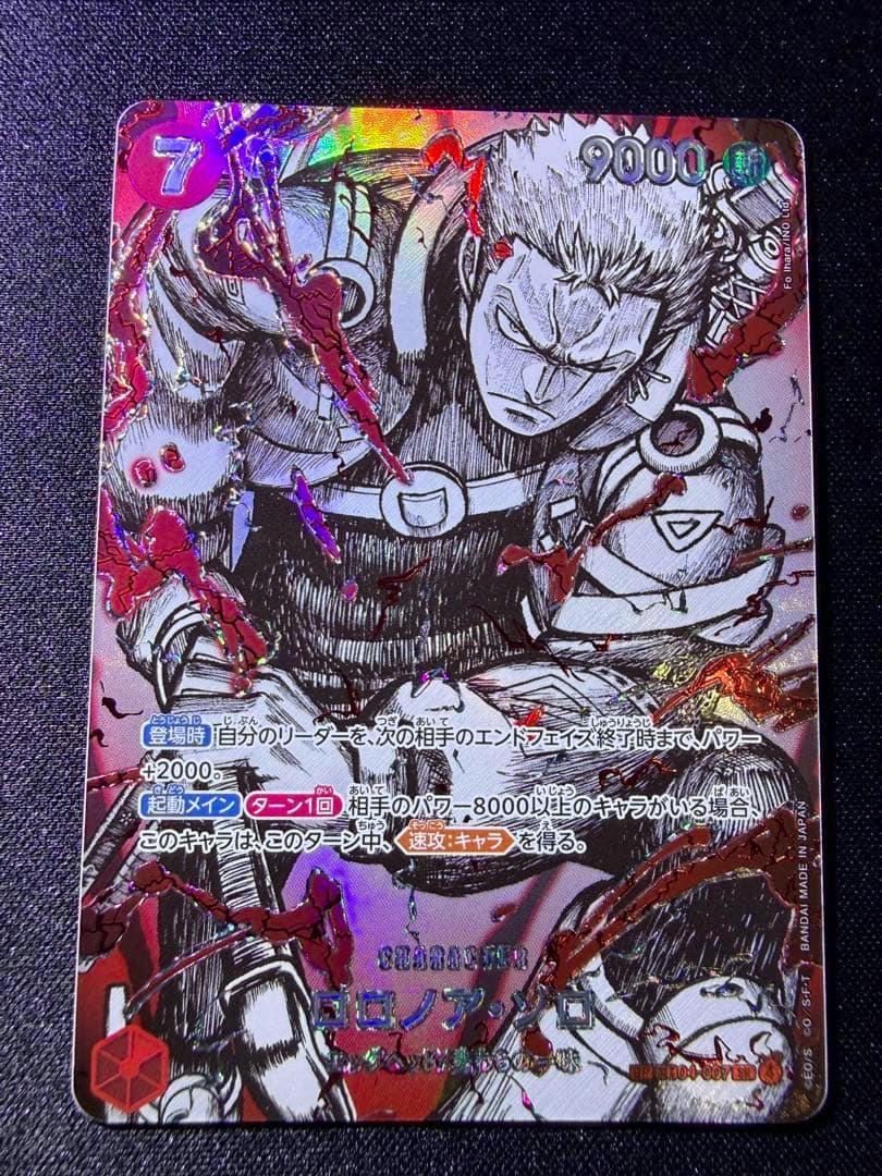 Photograph of a holographic trading card showing Roronoa Zoro with Japanese text and foil embellishments on a dark textured background.