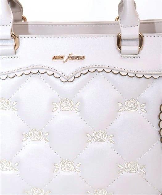 Close-up front view of a white quilted synthetic-leather bag with embroidered rose motifs and top handles.