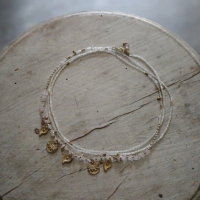 A rose quartz and Indian brass beaded necklace with small charms arranged in a circle on a wooden surface.