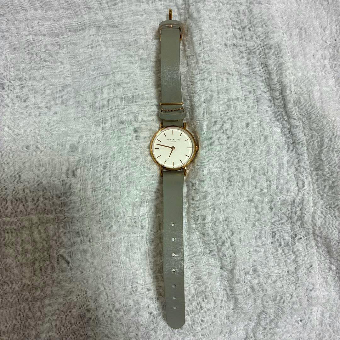Front view of a Rosefield wristwatch with a round white dial and grey leather strap laid flat on a white textured fabric.