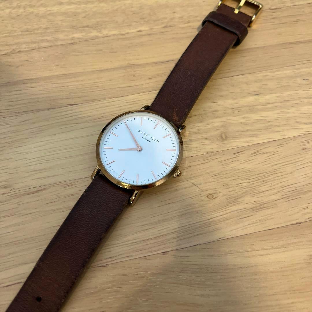ROSEFIELD watch with a white dial and brown leather strap lying on a wooden surface.