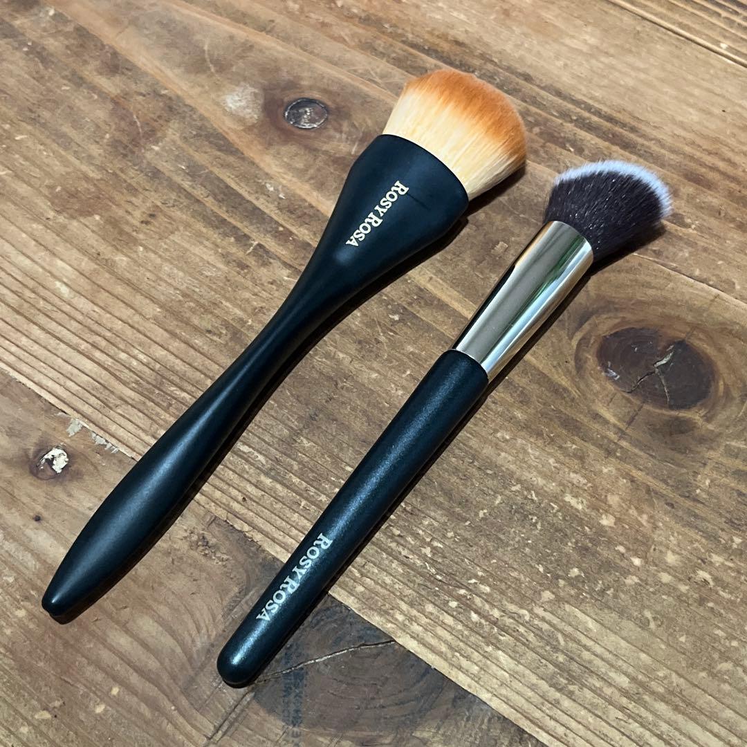 Two ROSY ROSA makeup brushes (two-piece set) laid on a wooden surface showing handles and brush heads.