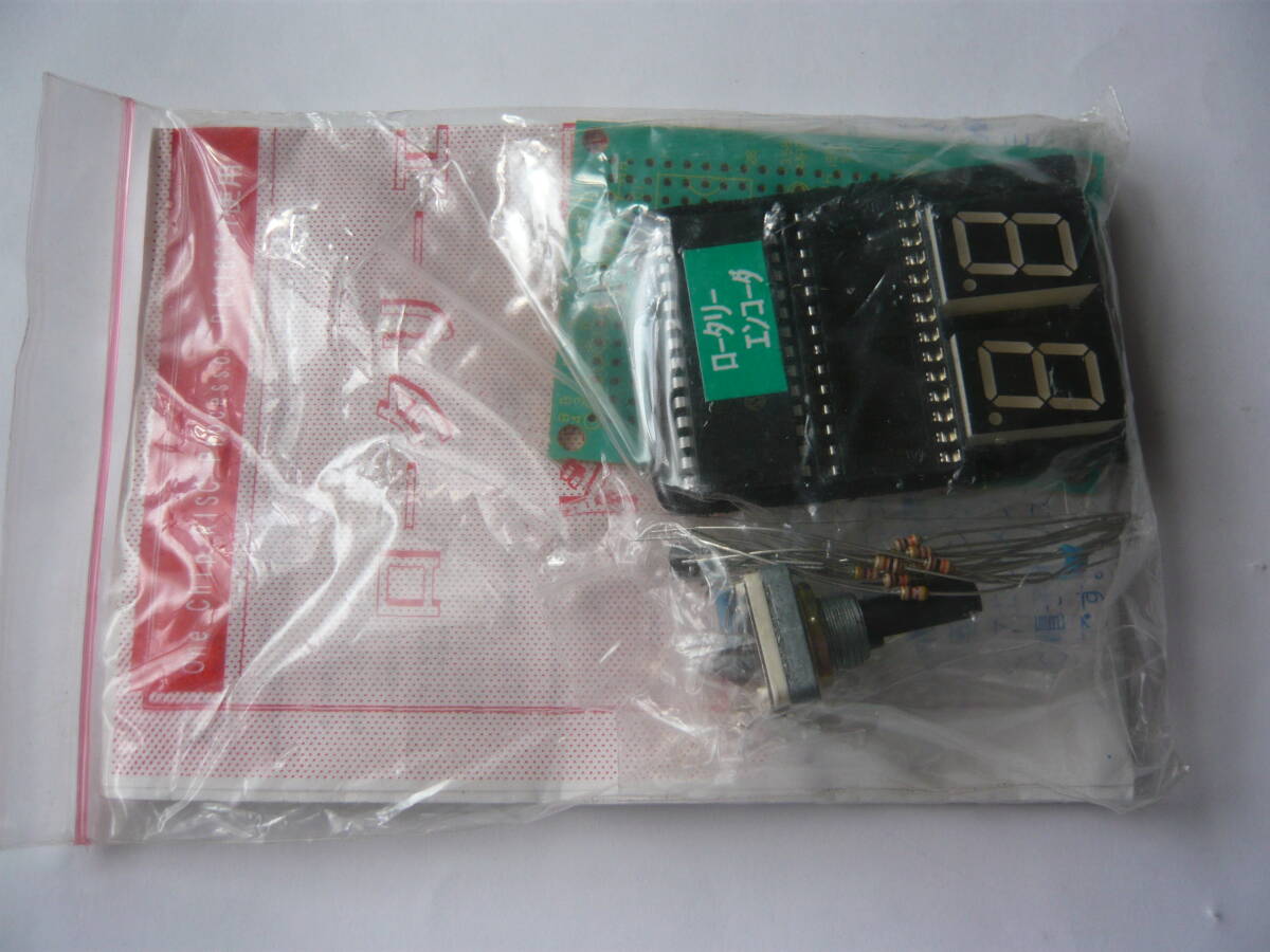 Sealed plastic bag showing the rotary encoder drive circuit kit components including a PCB, two 7-segment displays, resistors, and a rotary encoder.