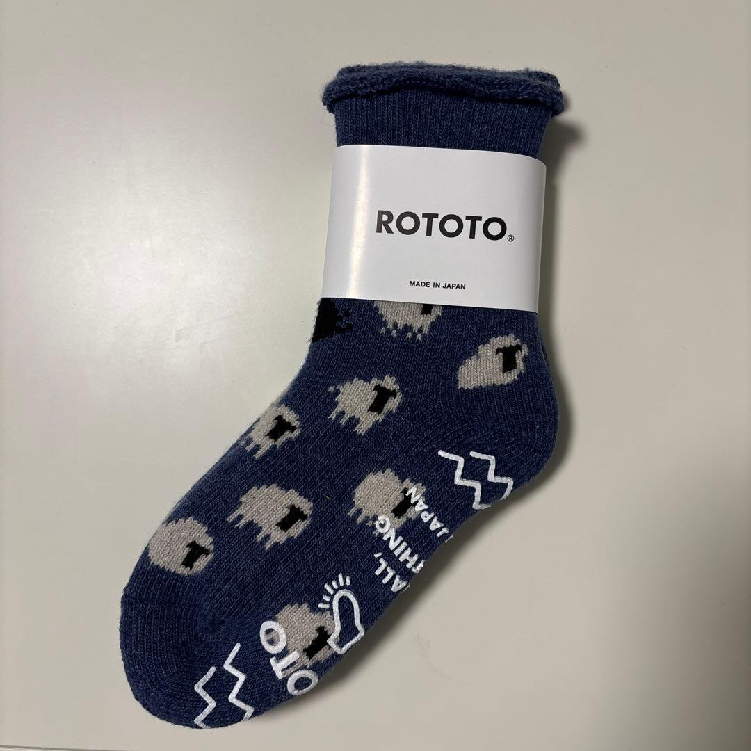 Blue ROTOTO wool room sock with sheep pattern and a white ROTOTO paper tag, shown flat.