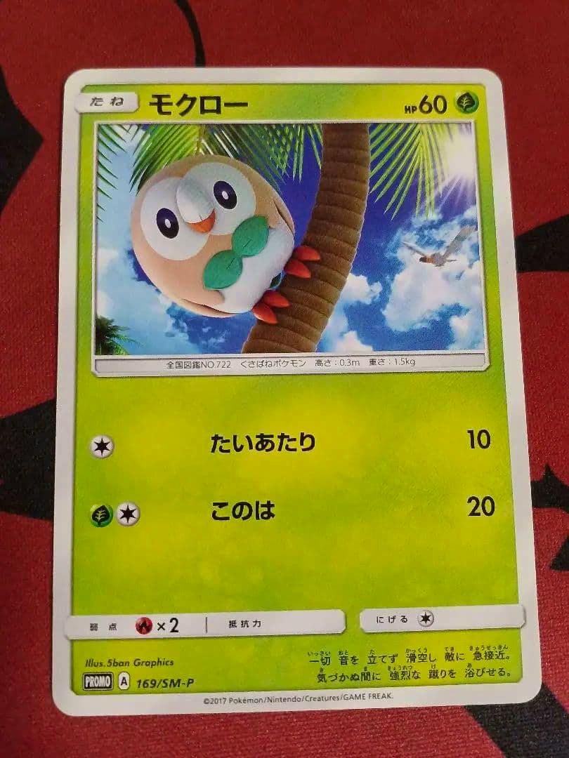 Front of the Japanese モクロー (Rowlet) promo trading card 169/SM-P photographed on a red background.