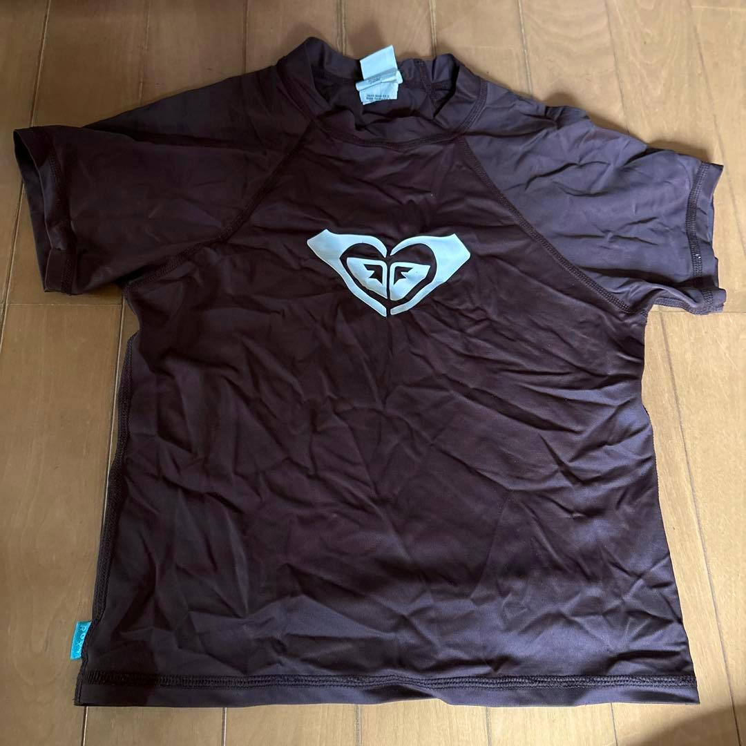 Brown ROXY rash guard laid flat showing the front with a white heart-shaped ROXY logo centered on the chest.