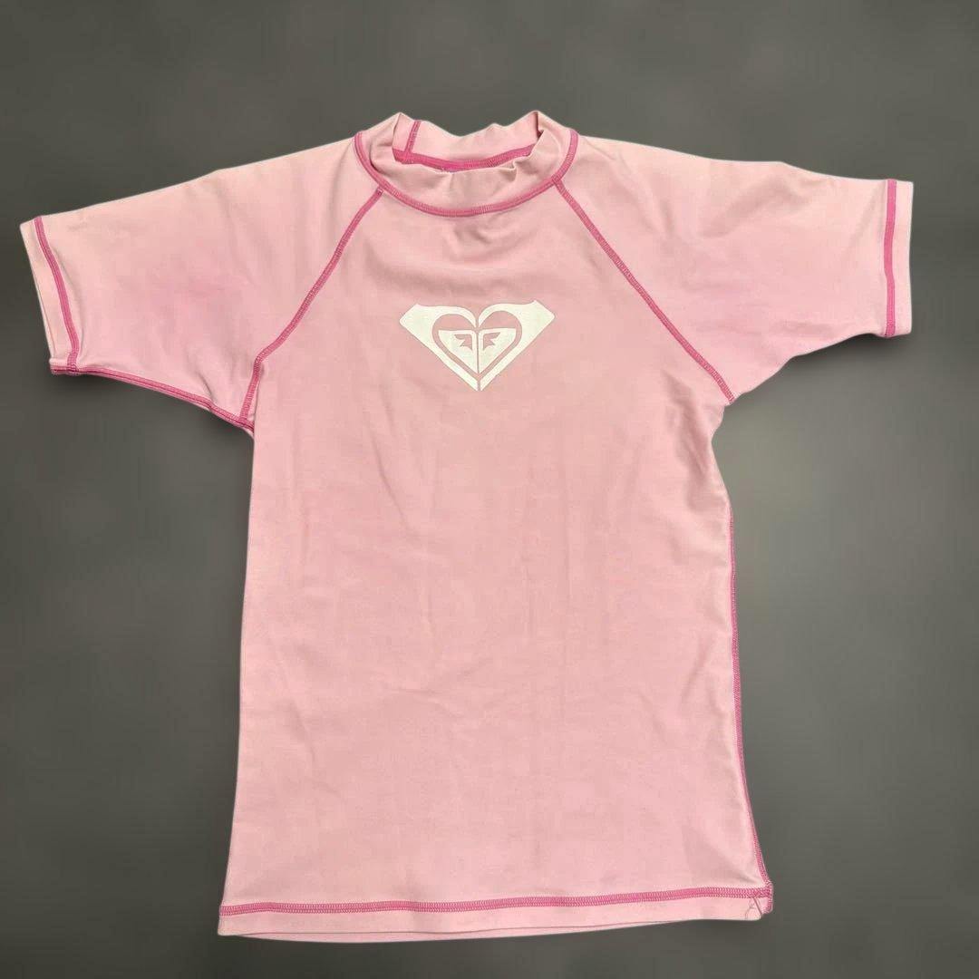 Pink ROXY short-sleeve rash guard laid flat showing the front with a white chest logo.