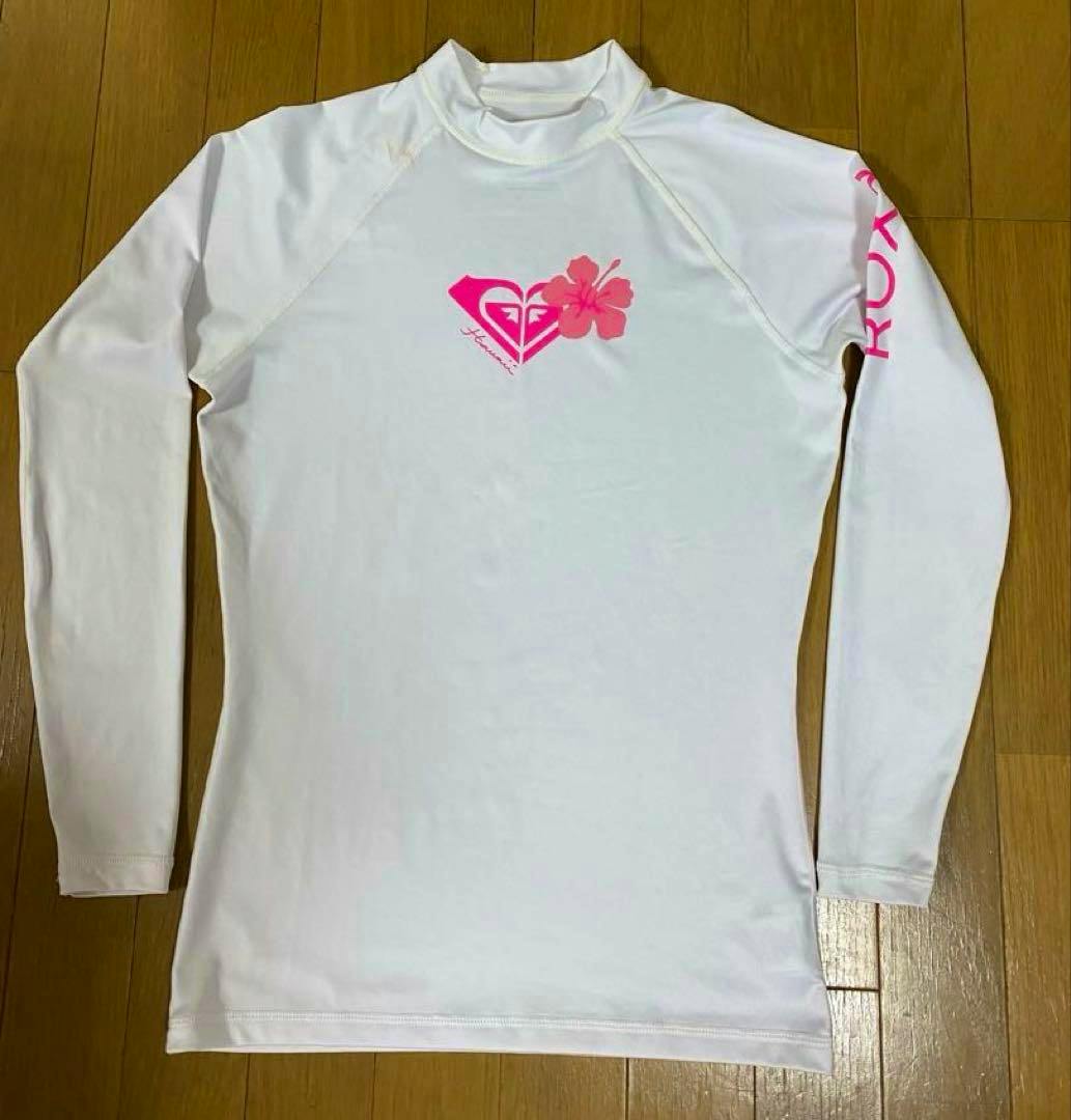 White ROXY rash guard (size L) laid flat showing a pink heart logo and hibiscus on the chest and pink ROXY text on the sleeve.