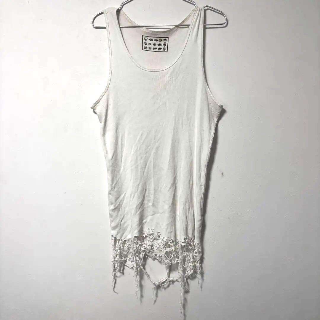 White distressed cotton tank top hanging on a hanger against a plain wall, showing frayed hem details.