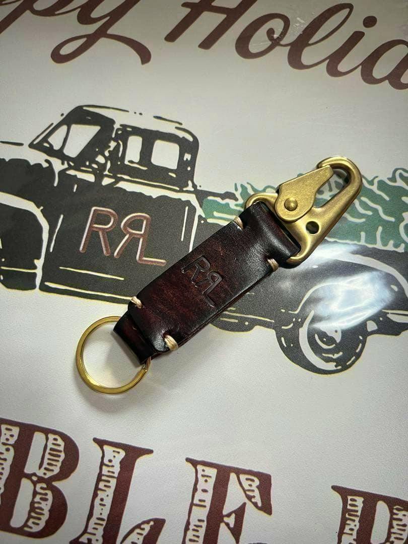 Dark brown RRL leather key hook keyholder with brass clip and brass key ring on a printed surface.
