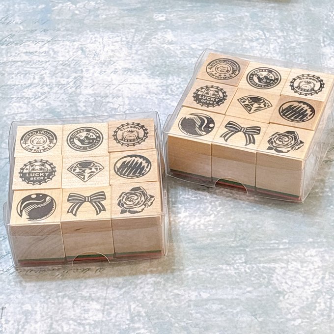 Two sets of wooden rubber stamps in clear plastic cases showing various stamp designs placed on a textured surface.