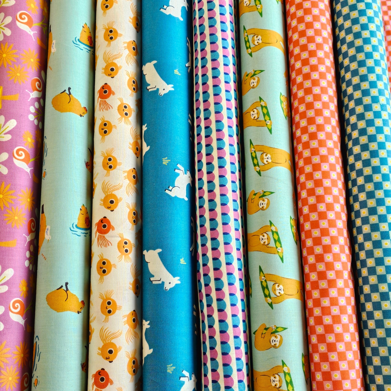 Several rolled bolts of printed cotton fabric showing colorful animal and geometric patterns.