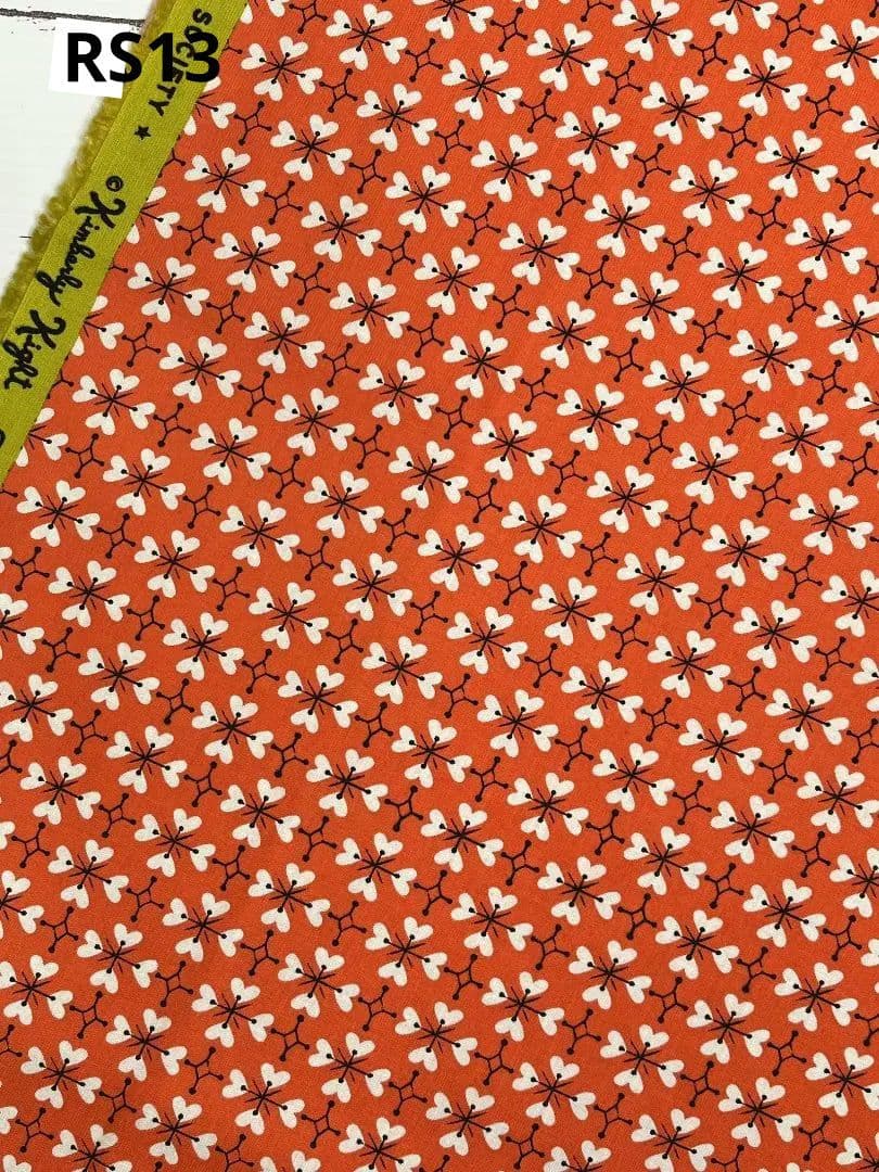 Red cotton fabric showing a repeating white heart-clover pattern and a green selvage with printed text.