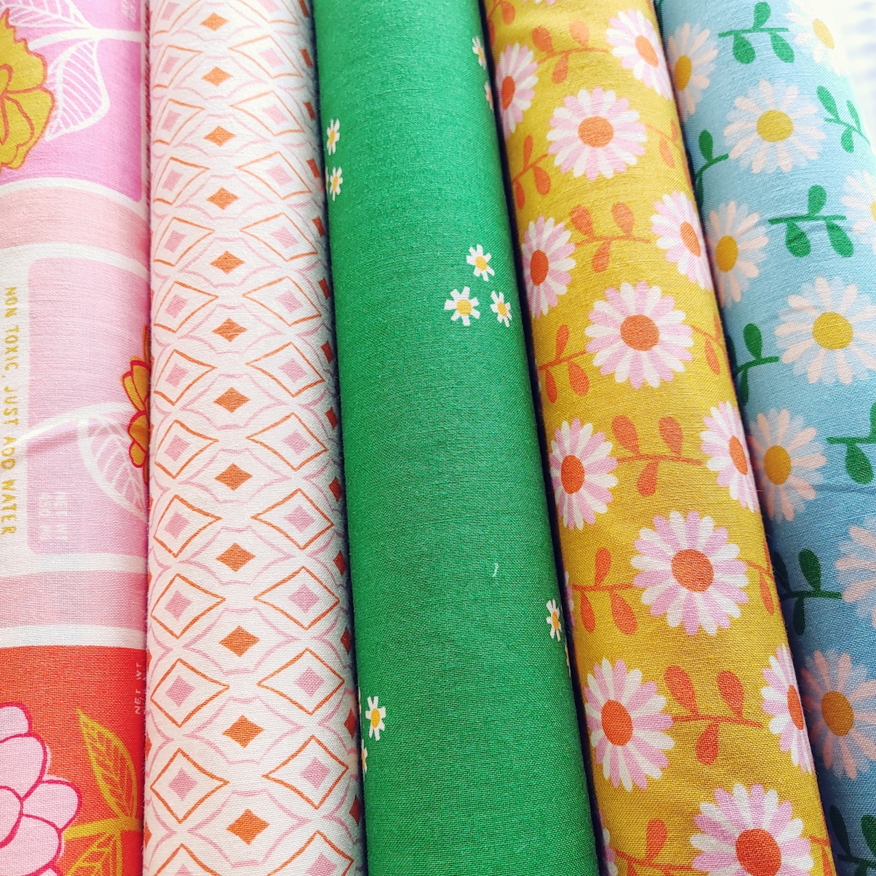 Rolled cotton fabric bolts showing Moda Flowerland floral and geometric patterns in multiple colors.