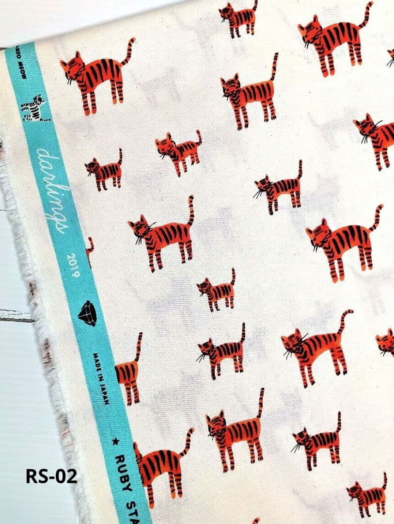 Cotton fabric with a repeating orange striped cat print and a turquoise selvedge with printed text.