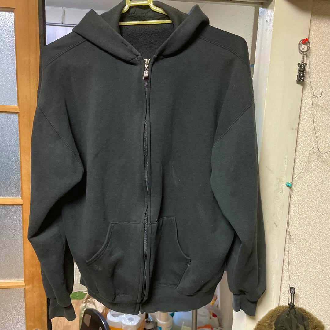 Black Russell Athletic zip-up hoodie hanging on a hanger against a doorway.