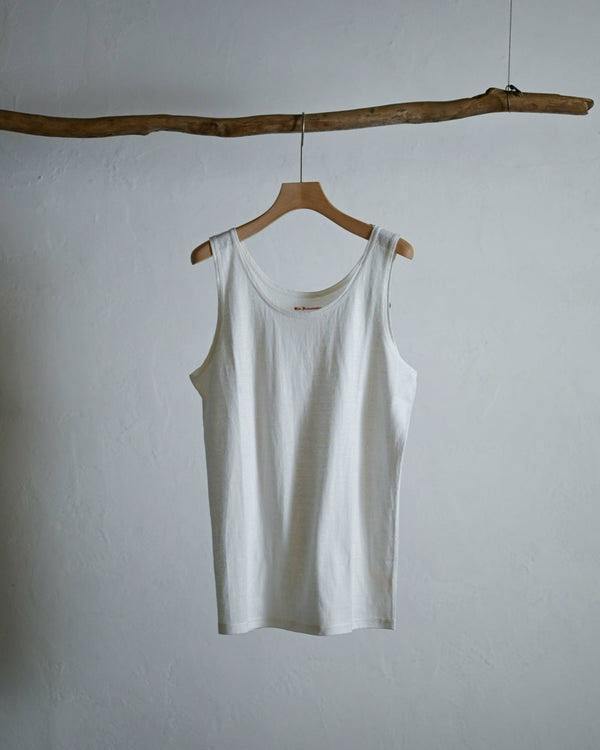White cotton sleeveless athletic singlet hanging on a wooden hanger against a plain wall.