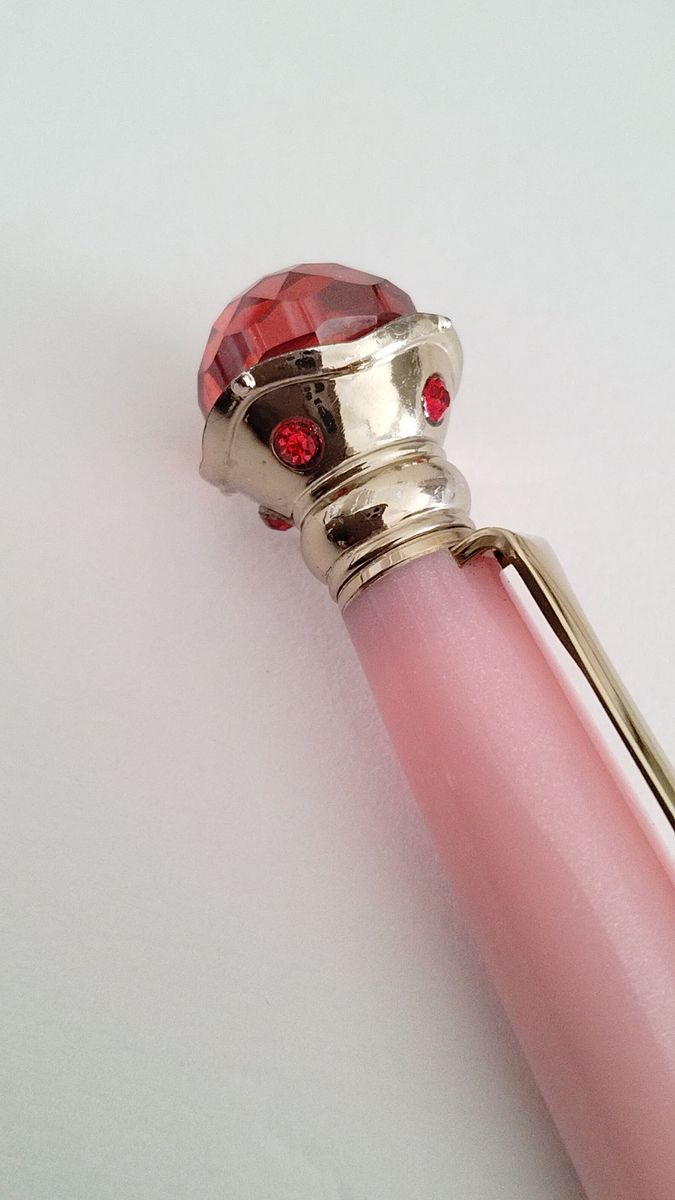 Close-up of a pink fountain pen cap with a faceted red jewel and gold-colored trim.