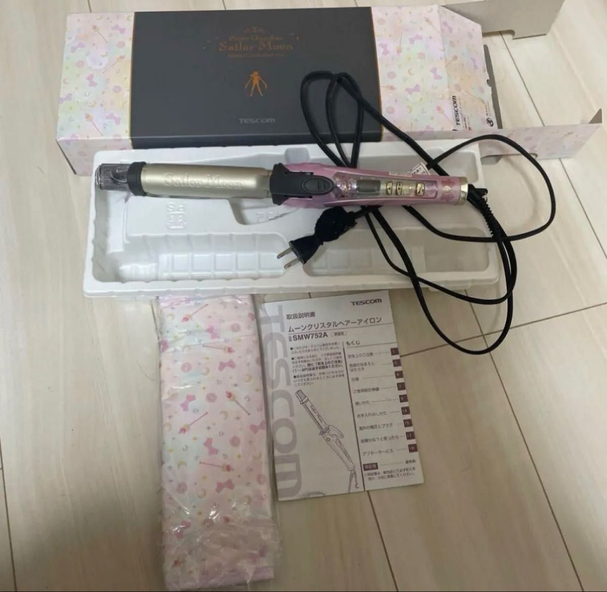 Pink Sailor Moon Tescom hair curling iron with its box, pouch, and manual on a wooden floor.