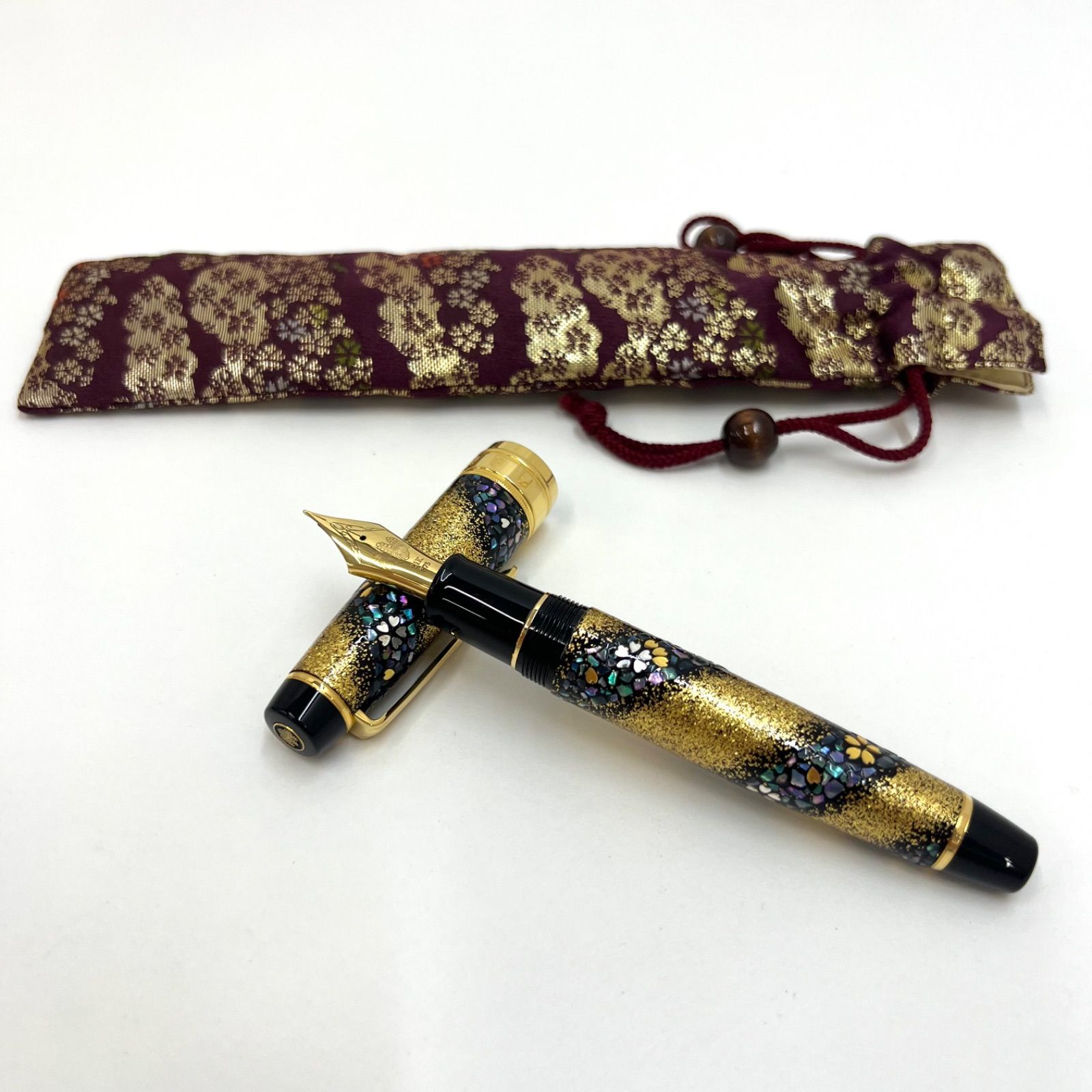 A SAILOR maki-e fountain pen with its cap off displayed crossed in front of a patterned fabric pen pouch.