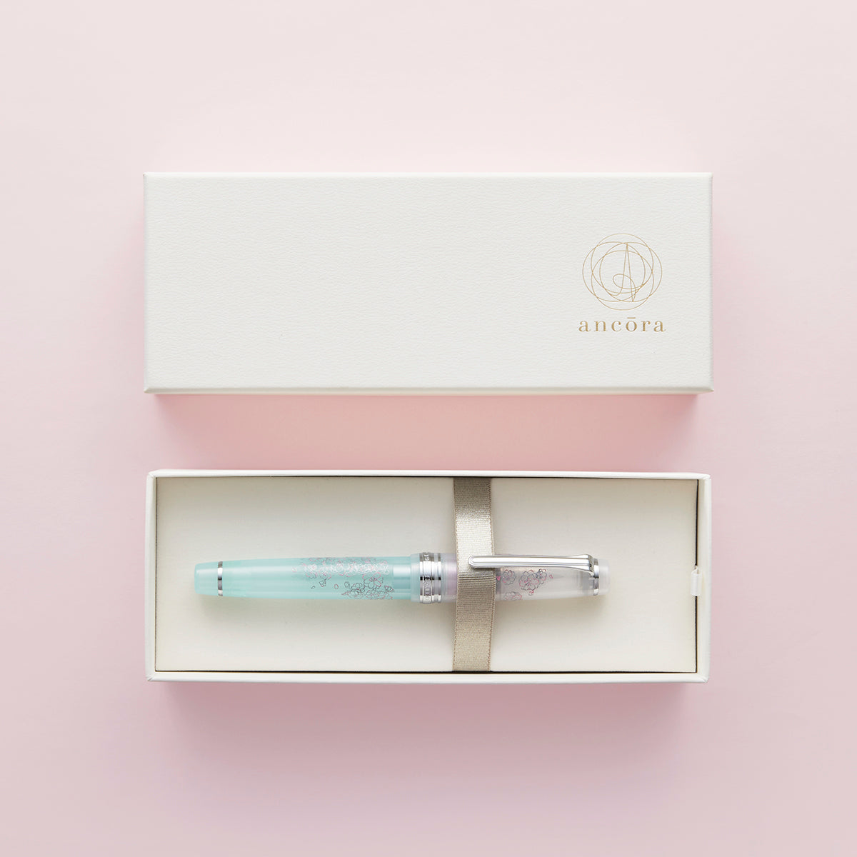 A fountain pen displayed in a white presentation box on a pink background.