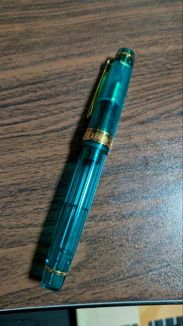 Sailor Professional Gear turquoise transparent fountain pen capped and resting on a wood surface.