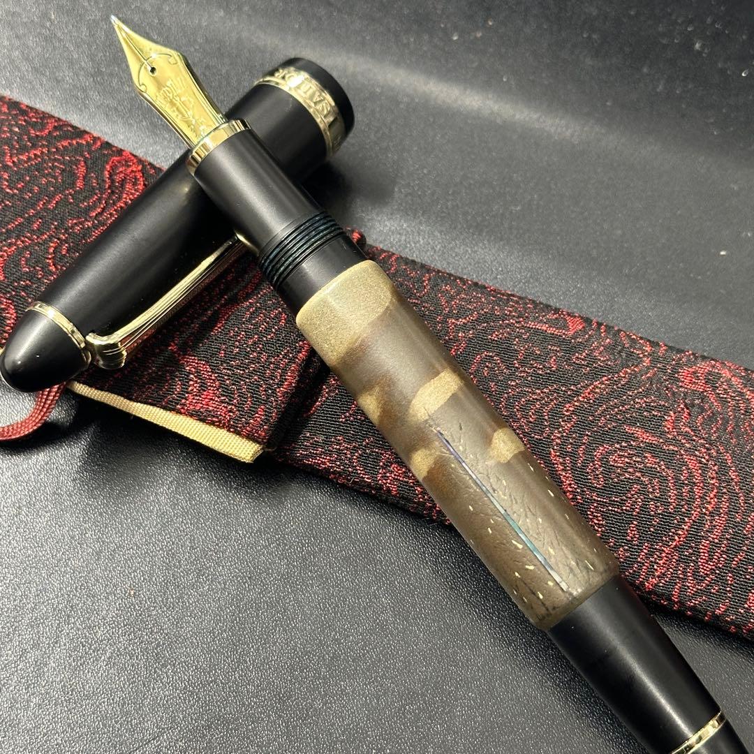 Fountain pen with the cap removed showing a gold nib and a lacquered barrel with raden (mother-of-pearl) inlay resting on a black surface and red patterned cloth.