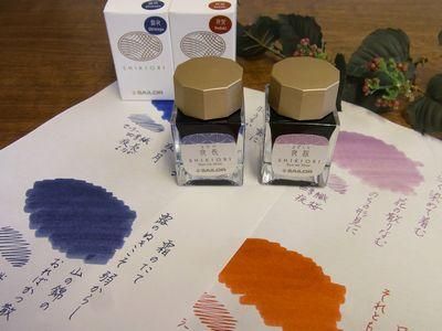 Two Sailor SHIKIORI fountain pen ink bottles with their boxes placed on paper showing ink swatches and handwriting.