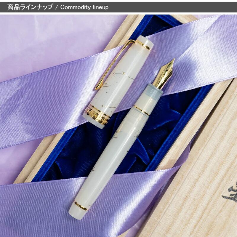 White fountain pen uncapped, showing the gold-colored nib, placed on a purple ribbon and a wooden presentation box.