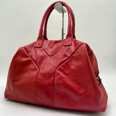 Red leather bag with top handles displayed on a stand against a white background.