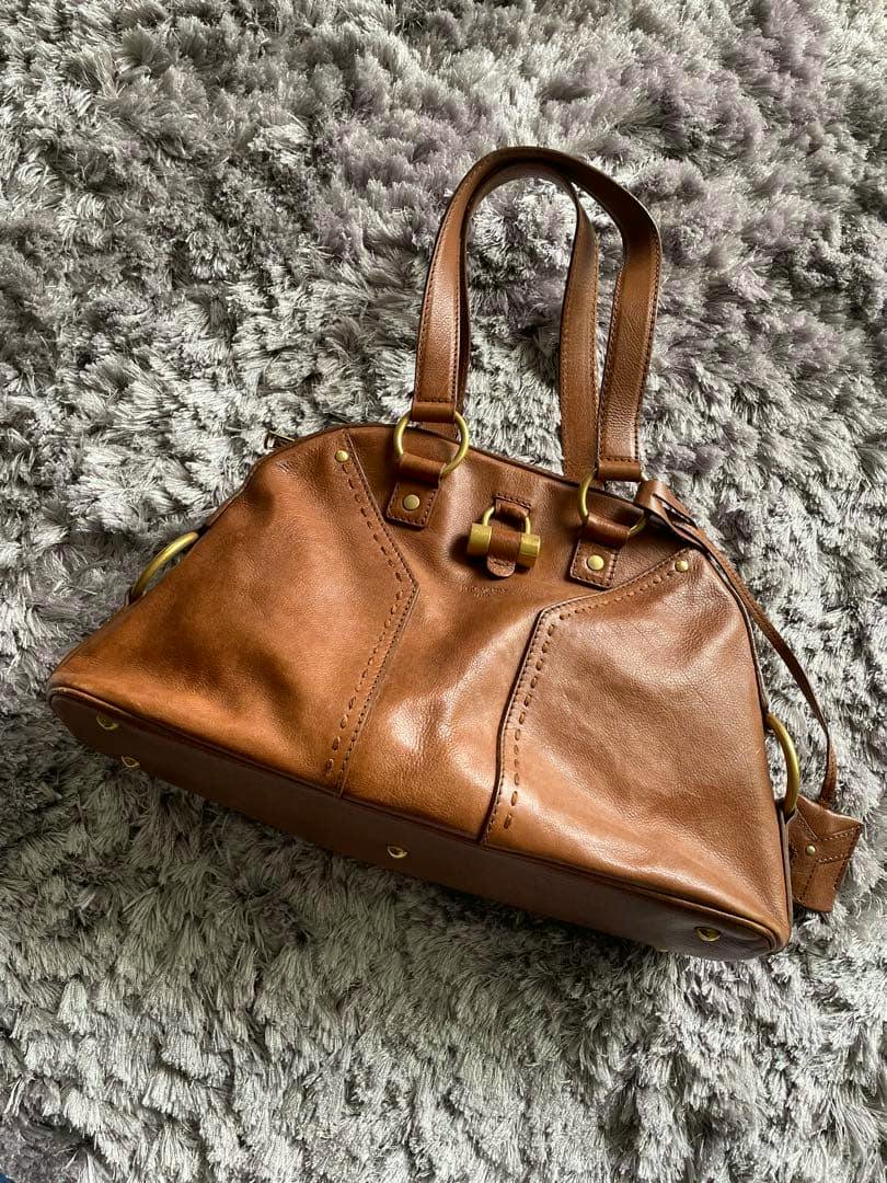 Brown cow leather Yves Saint Laurent Muse bag shown on a gray shag rug, front and handles visible.