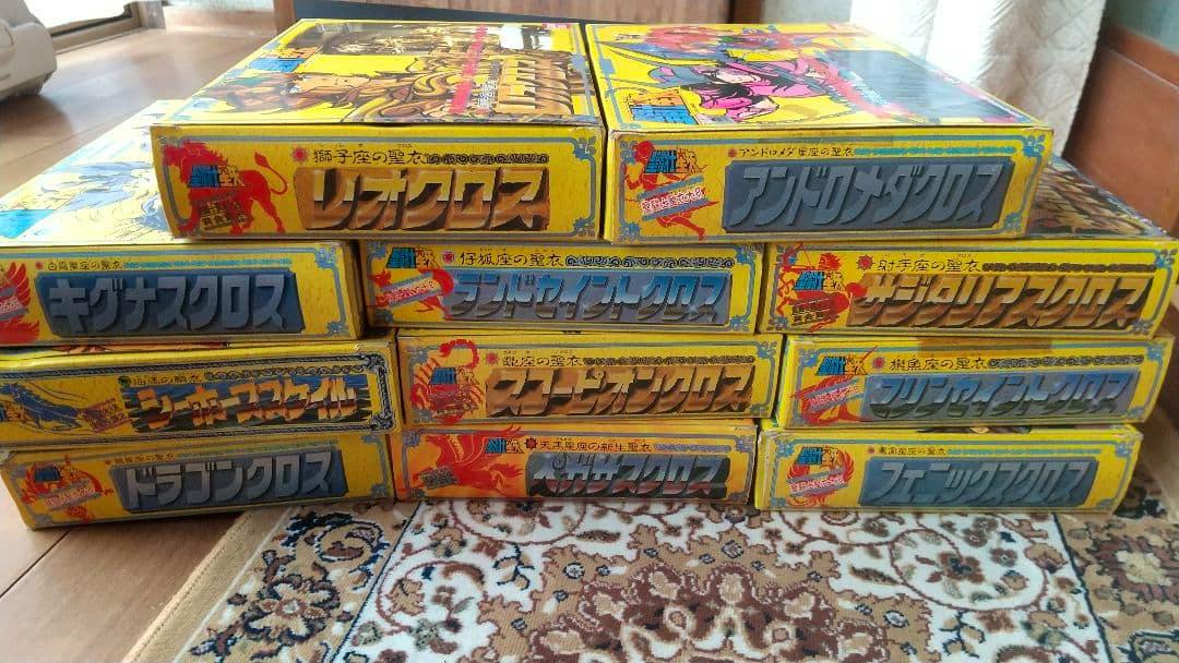 Stacked yellow boxes of 聖闘士星矢 聖闘士聖衣大系 figure sets displayed on a floor rug.