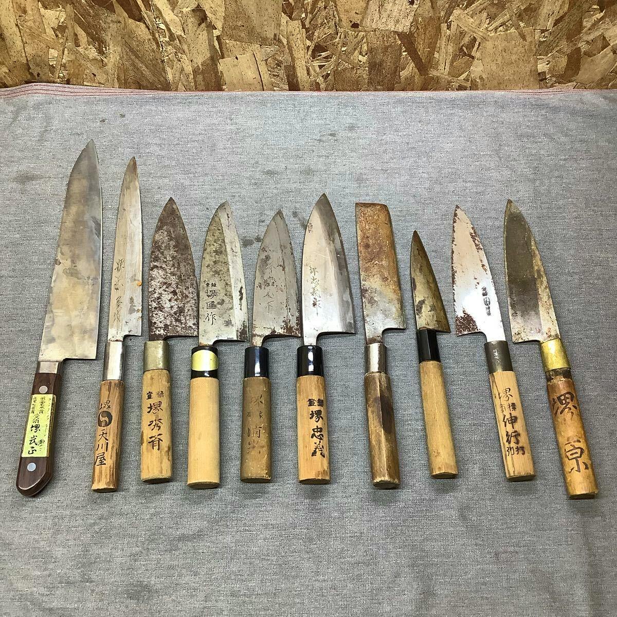 A row of Japanese chef knives with wooden handles laid out side by side on a fabric surface.