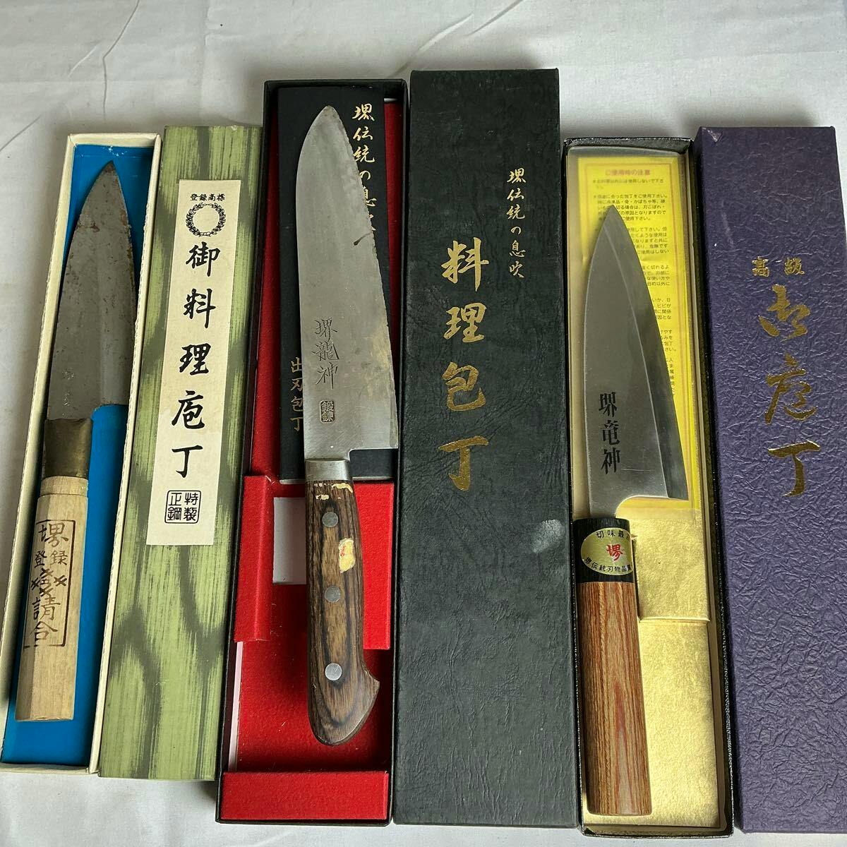Three Japanese chef knives in their boxes arranged side by side showing blades and handles.