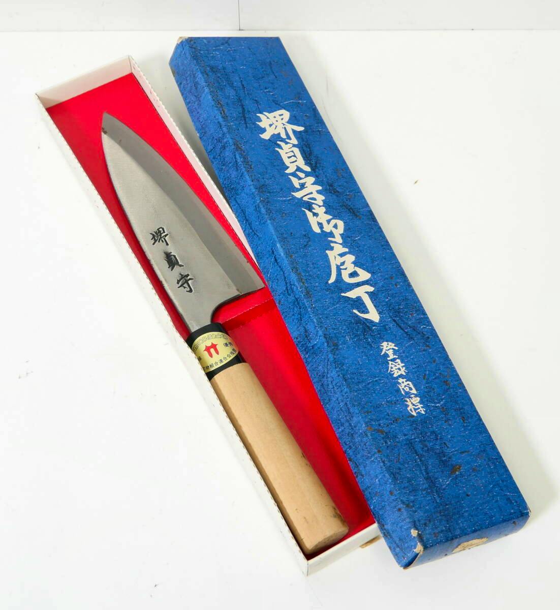 A Japanese deba-style chef knife with a wooden handle shown in an open presentation box with a blue outer lid bearing Japanese characters.