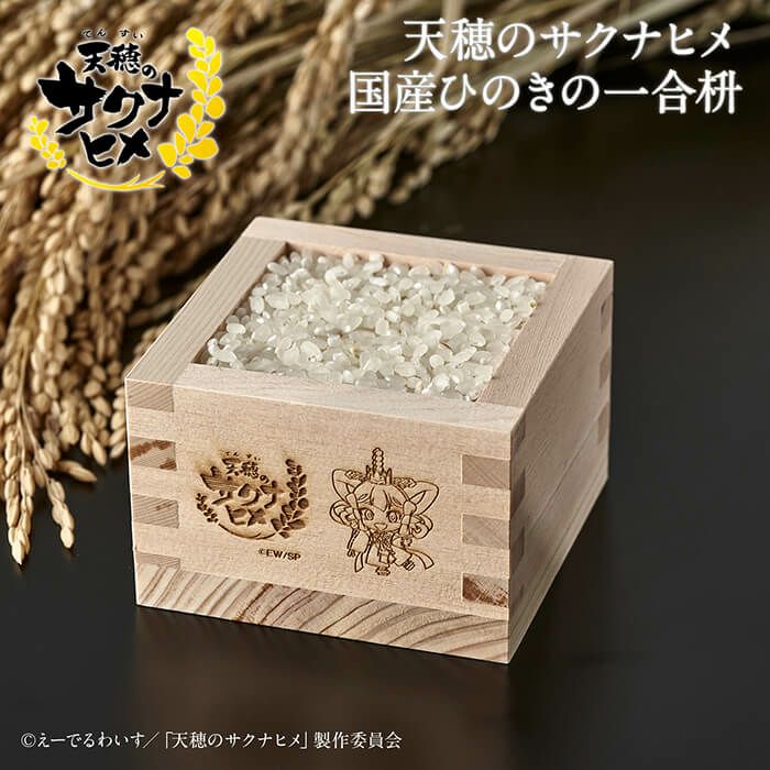 A domestic hinoki one-go masu engraved with Sakuna collaboration artwork, filled with rice and shown with rice stalks in the background.