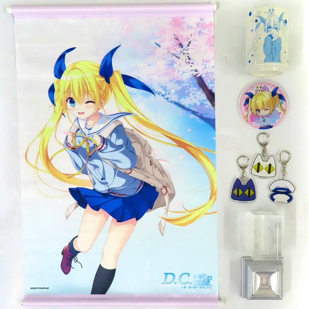 Flat-lay photo of the goods set showing a wall scroll of 芳乃さくら, a round badge, three small acrylic keychains, a cylindrical cup, and a 3D crystal display.