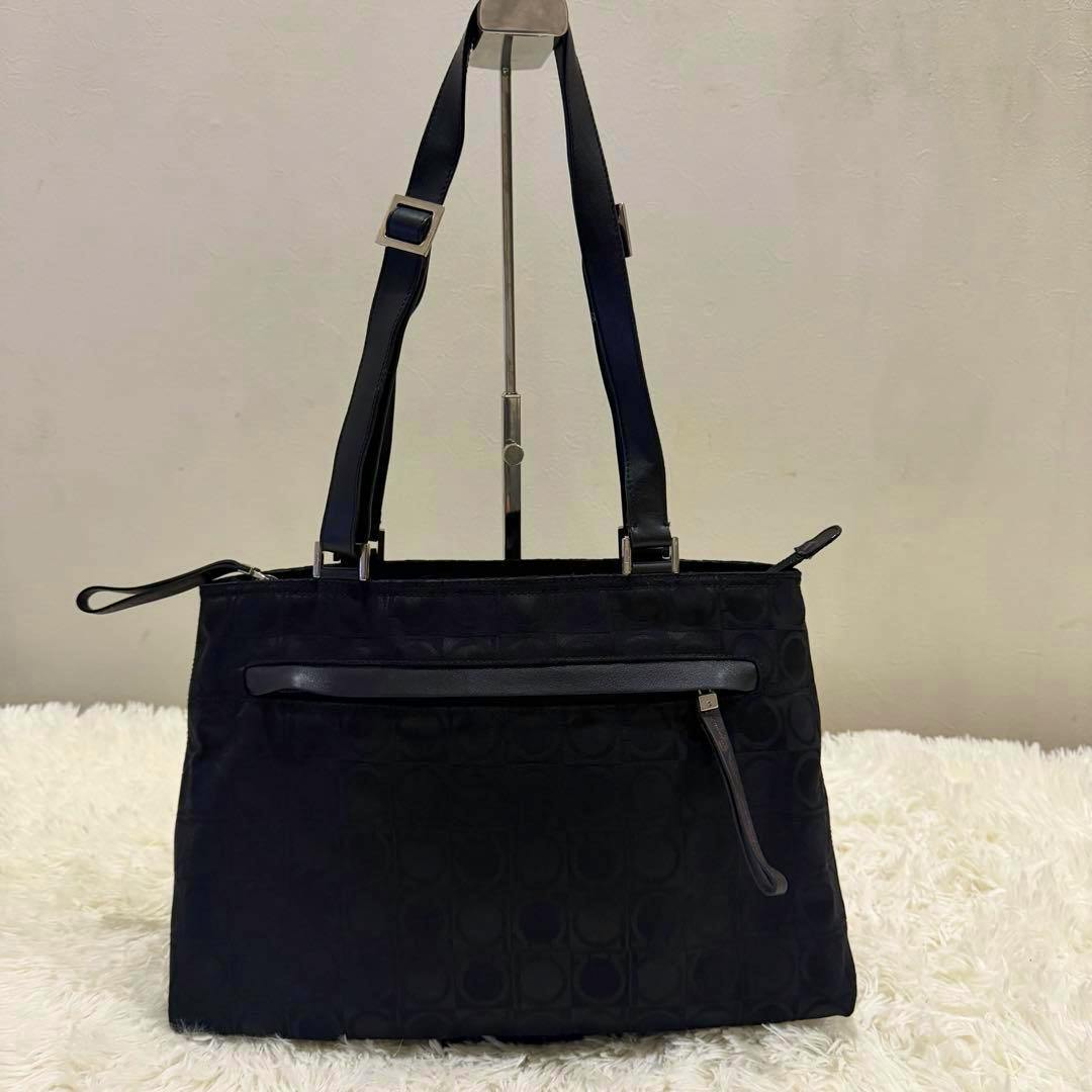 Front view of a black Salvatore Ferragamo Gancini-pattern tote bag with two shoulder straps and a front zip pocket.