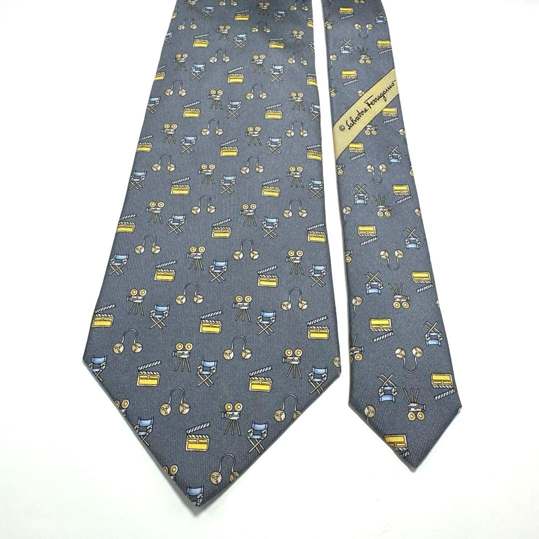 Full gray Salvatore Ferragamo silk necktie laid flat showing small repeating yellow and blue motifs and the brand label.