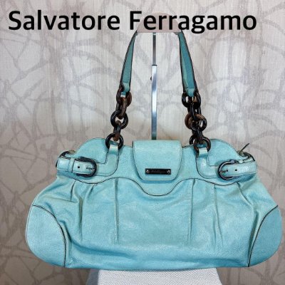 Turquoise leather Salvatore Ferragamo handbag with two shoulder straps displayed on a stand.