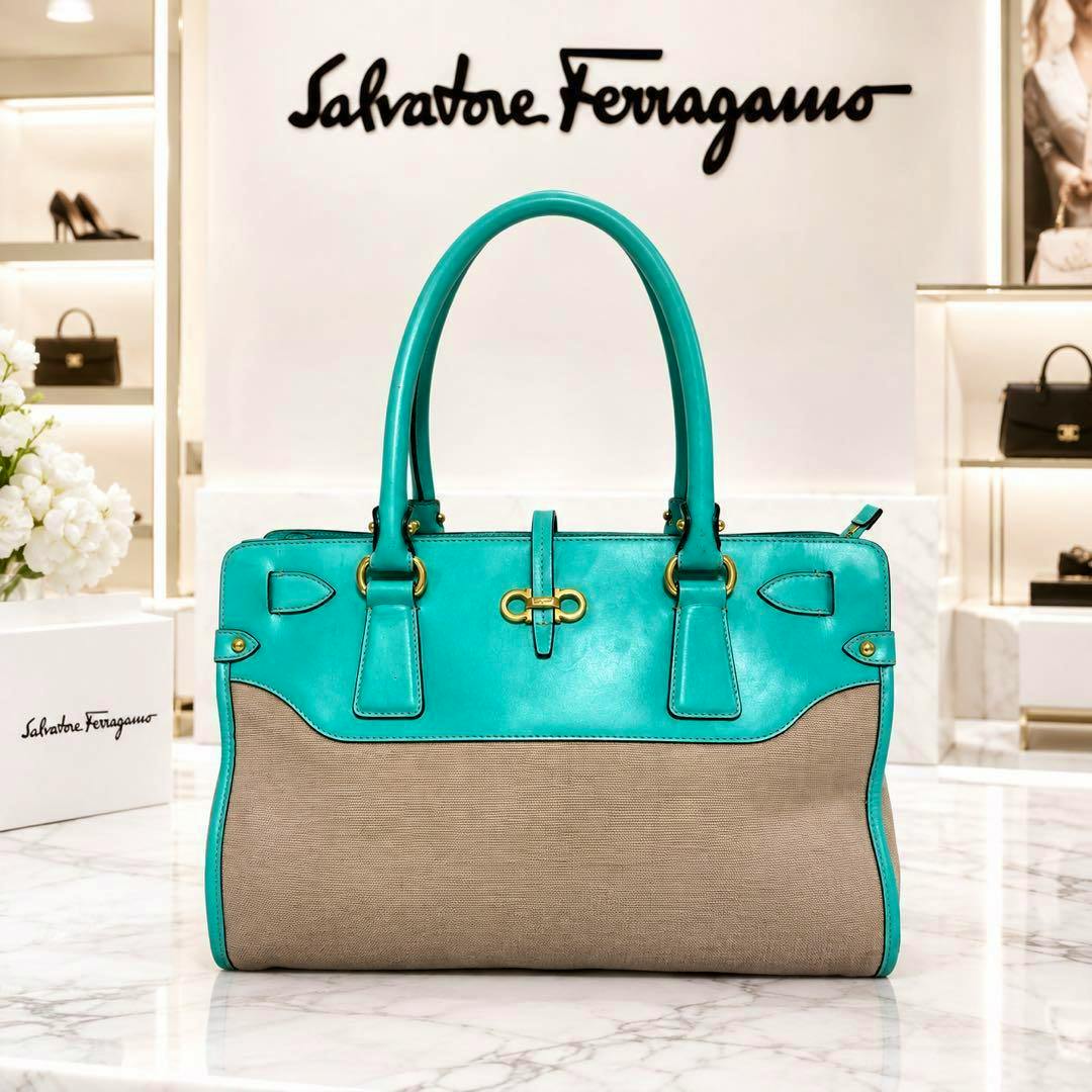 Front view of a turquoise and beige Salvatore Ferragamo tote handbag placed on a marble surface in a store setting.