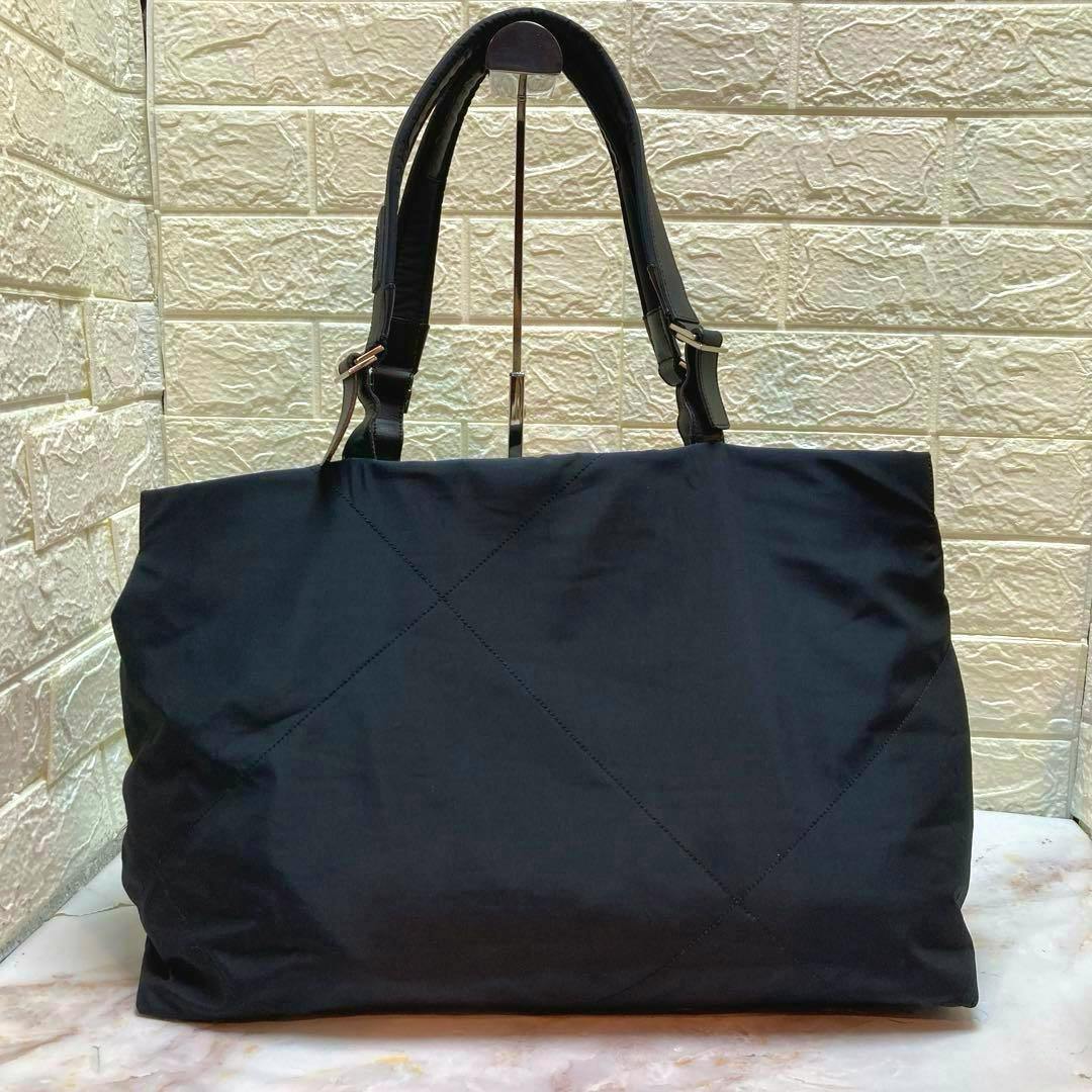 Front view of a black nylon Ferragamo tote bag with shoulder straps against a textured wall.