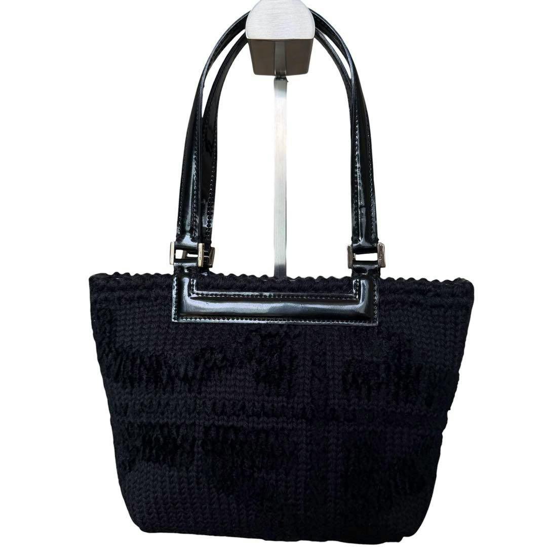 Black pile-textile Salvatore Ferragamo handbag with glossy black handles hanging on a display stand.