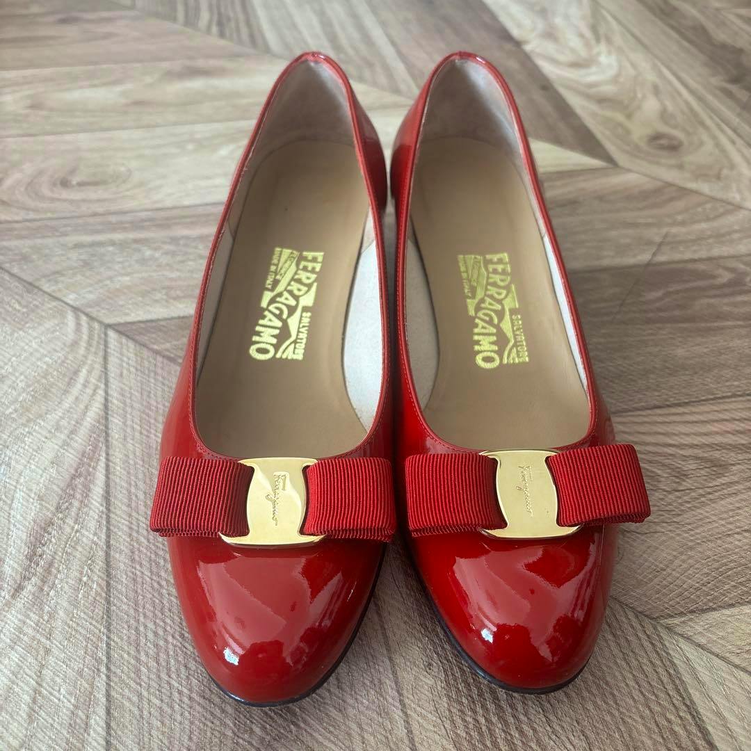 Top view of a pair of red Salvatore Ferragamo patent leather pumps with grosgrain bows and gold logo plates.