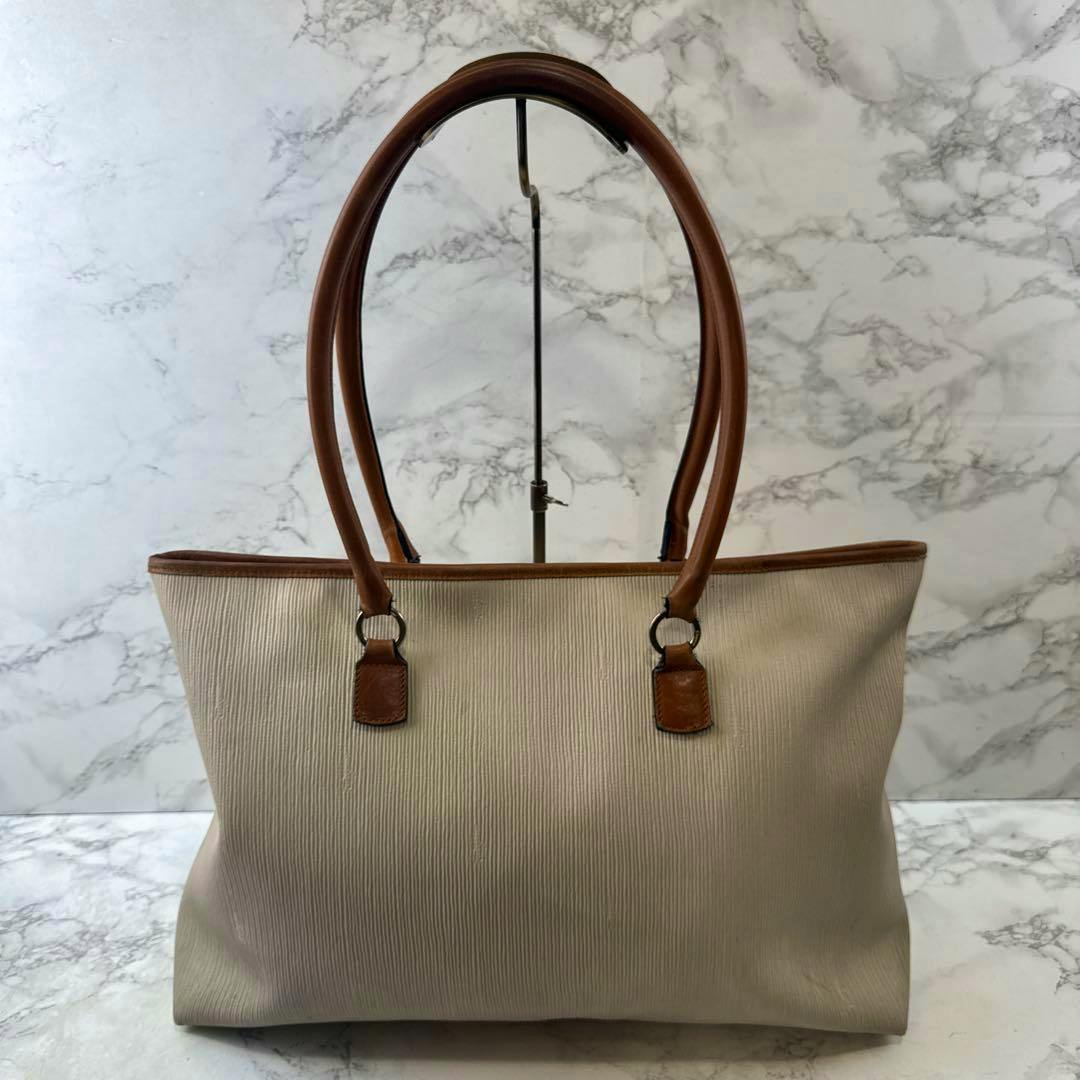 Front view of a Salvatore Ferragamo beige textured tote bag with brown leather handles.