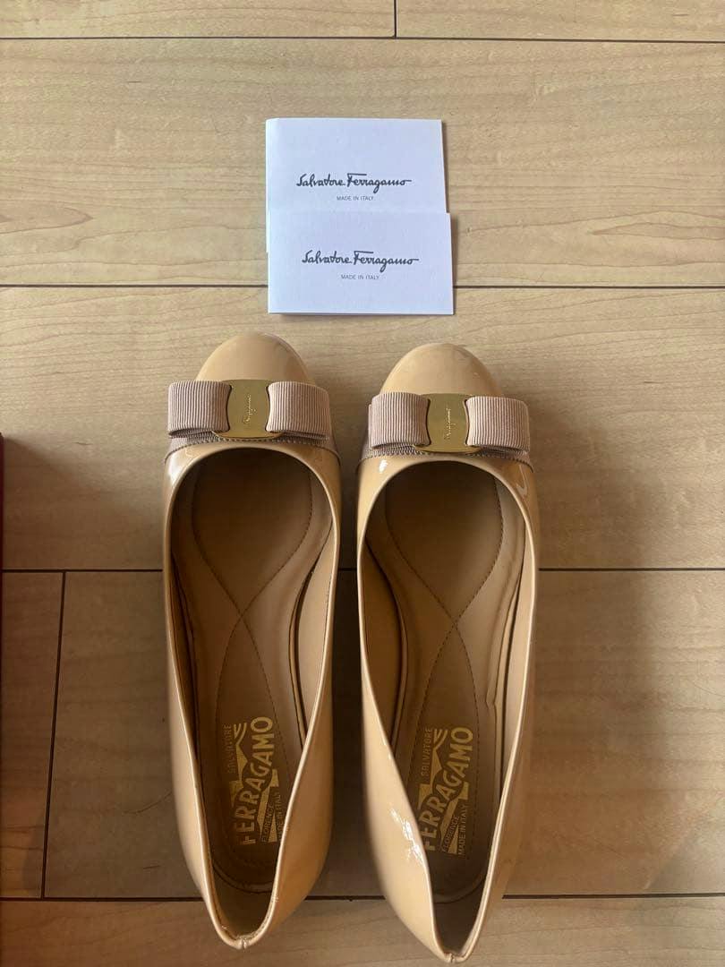 A pair of beige Salvatore Ferragamo Vara ribbon flat shoes shown from above on a wooden floor with two Ferragamo cards above them.
