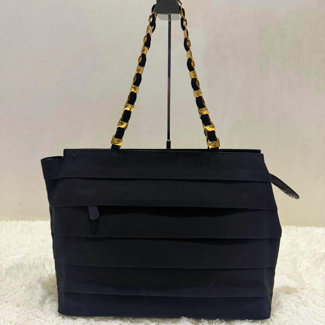 Front view of a black Salvatore Ferragamo Vara ribbon tote bag with gold chain-and-ribbon shoulder straps on a display stand.