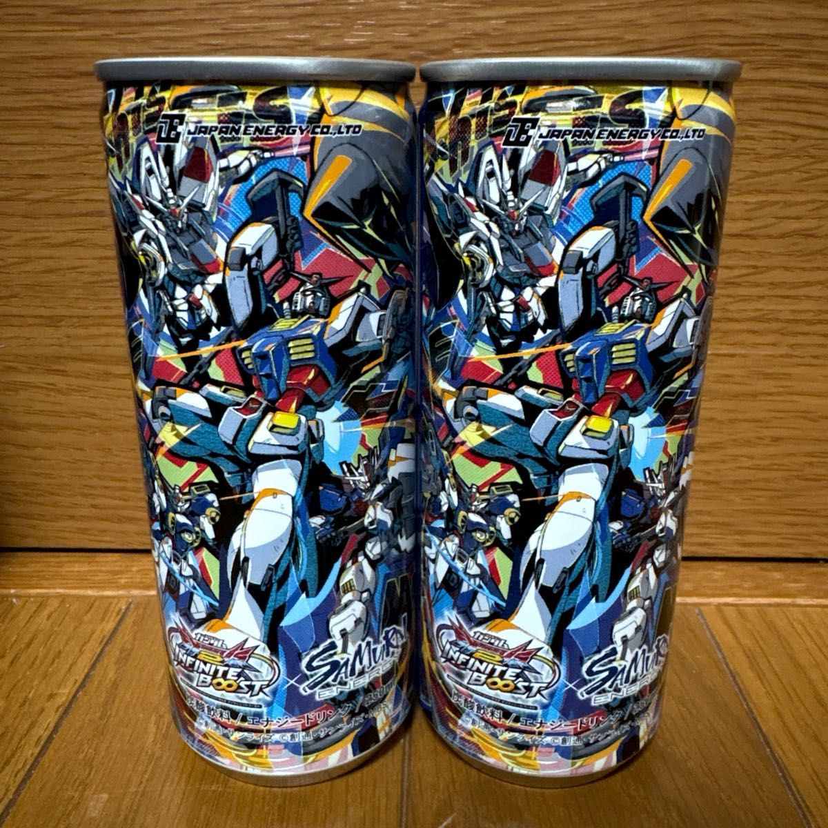 Two canned energy drinks with Gundam collaboration artwork standing side by side on a wooden surface.