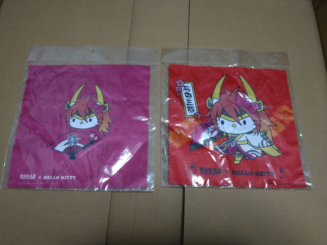 Two packaged polyester cleaning cloths from the Sengoku Musou4 × HELLO KITTY Ishida Mitsunari 2-piece set, showing printed character designs on pink and red backgrounds.